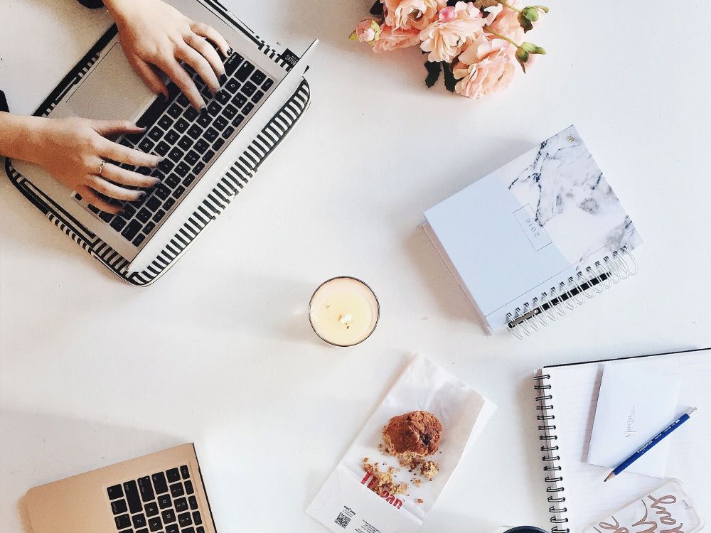 A pair of hands typing on a laptop on a white desk